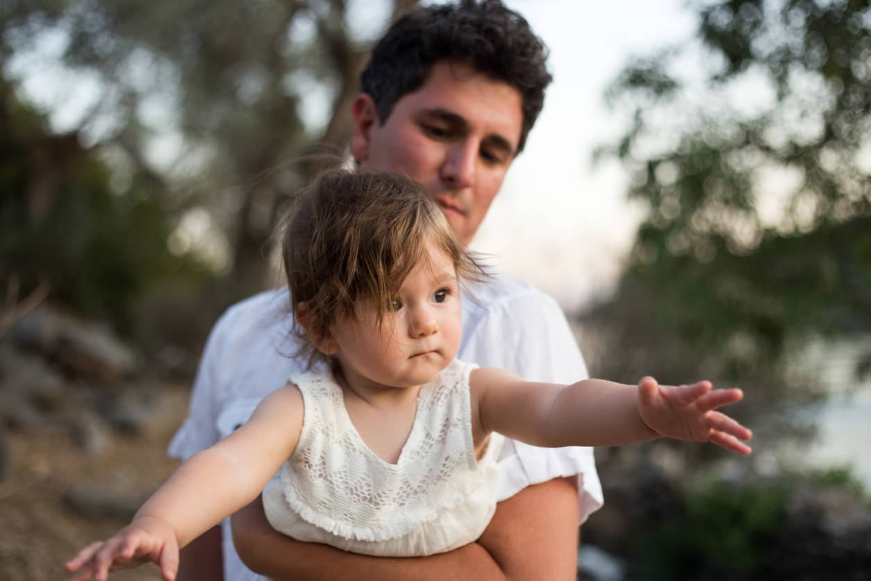 Father holding his daughter with her arms outstretched for mama.