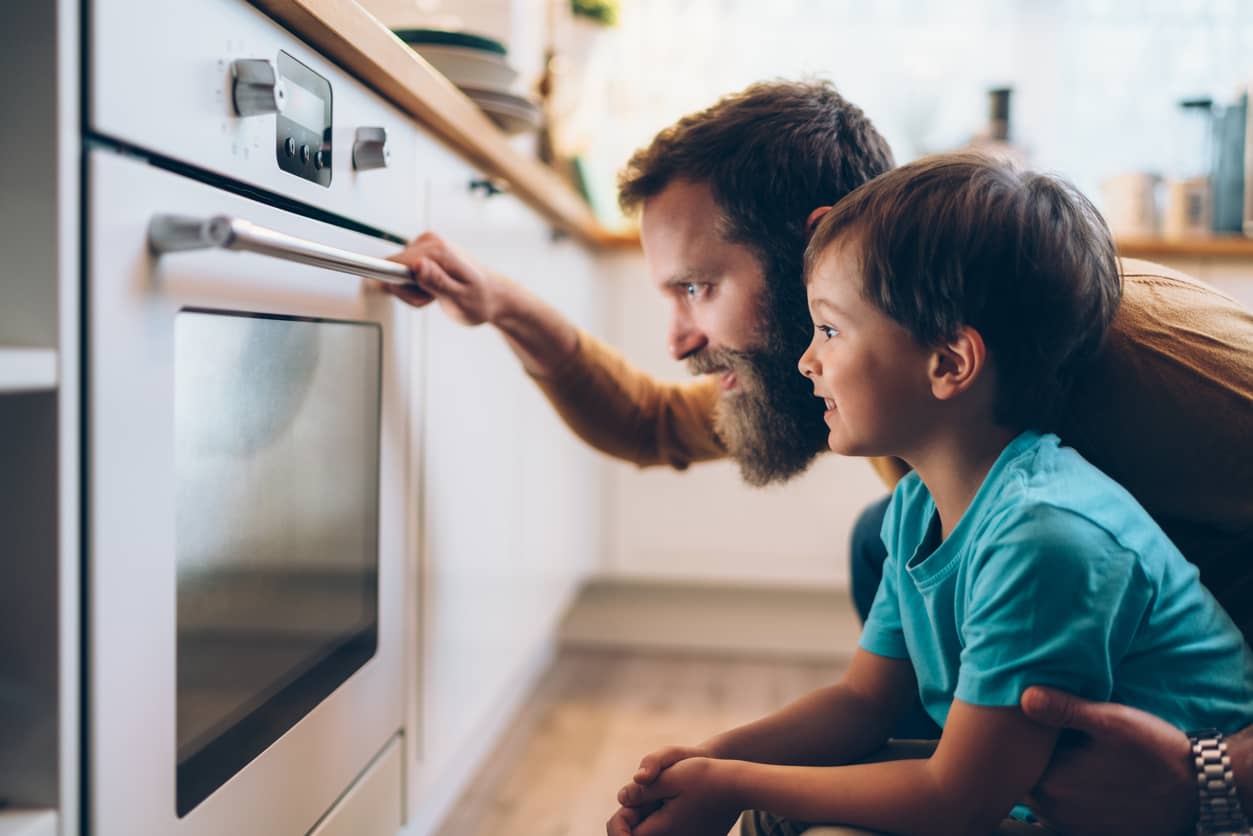 Father and son peering into the oven while cooking dinner. A father teaching a growth mindset.