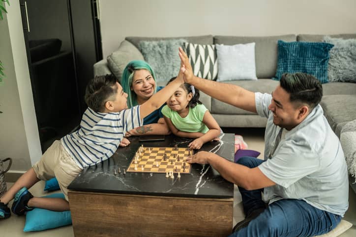 Father and son high-fiving while playing chess at home.