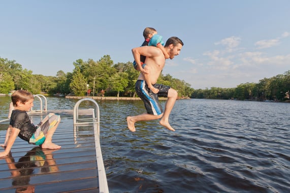 Father and two sons having fun and jumping in a lake on a hot day