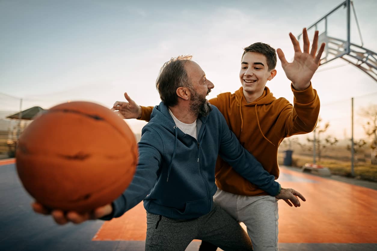 Father playing basketball with his teenage son, keeping the parent-teen connection.