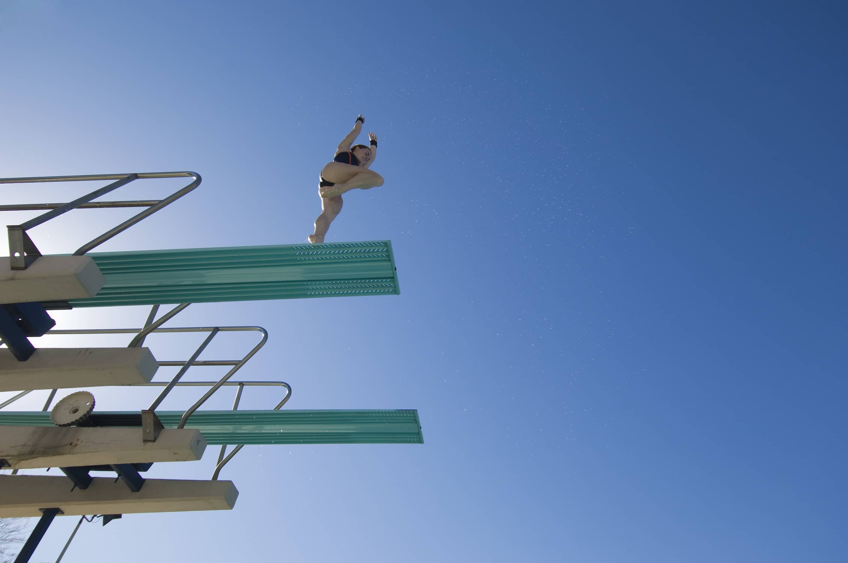 Woman approaching a dive on the high diving board with blue sky in the background.
