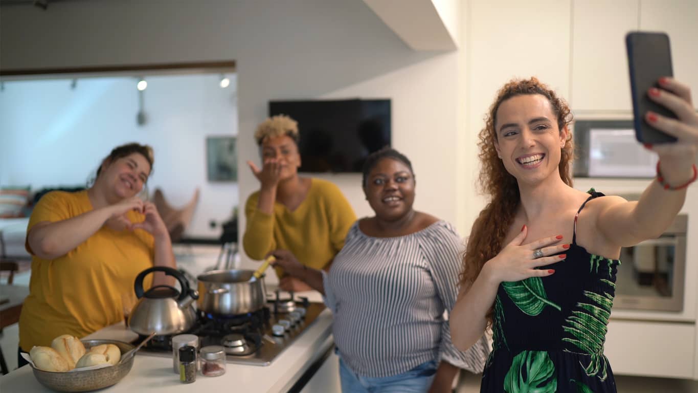 Friends gathered in the kitchen and facetiming on their smartphone.