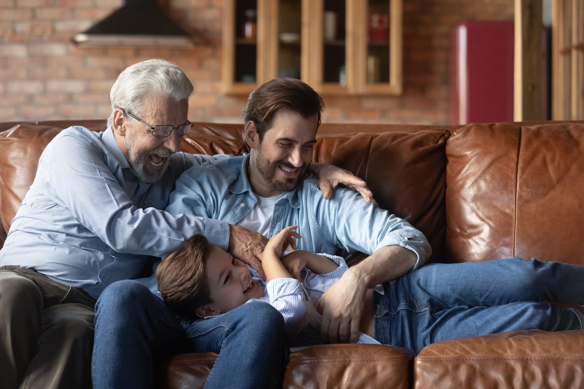 Funny playtime. Joyful elderly grandfather millennial dad tickle giggling tween kid boy on couch_AdobeStock_467664196_SM_Compressed