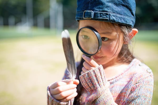 Young girl examining a feather with a magnifying glass