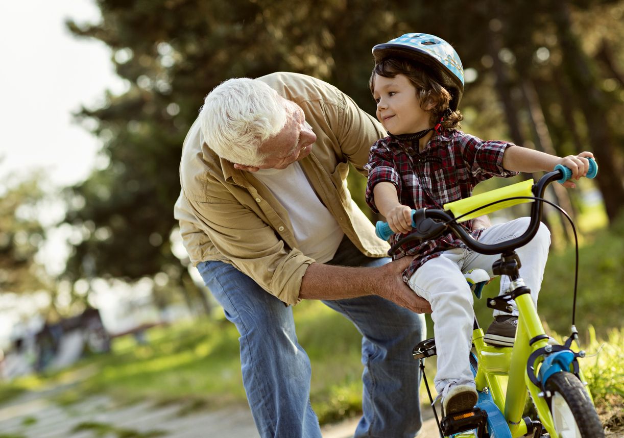 A grandfather helping a young high energy boy learn to ride a bike