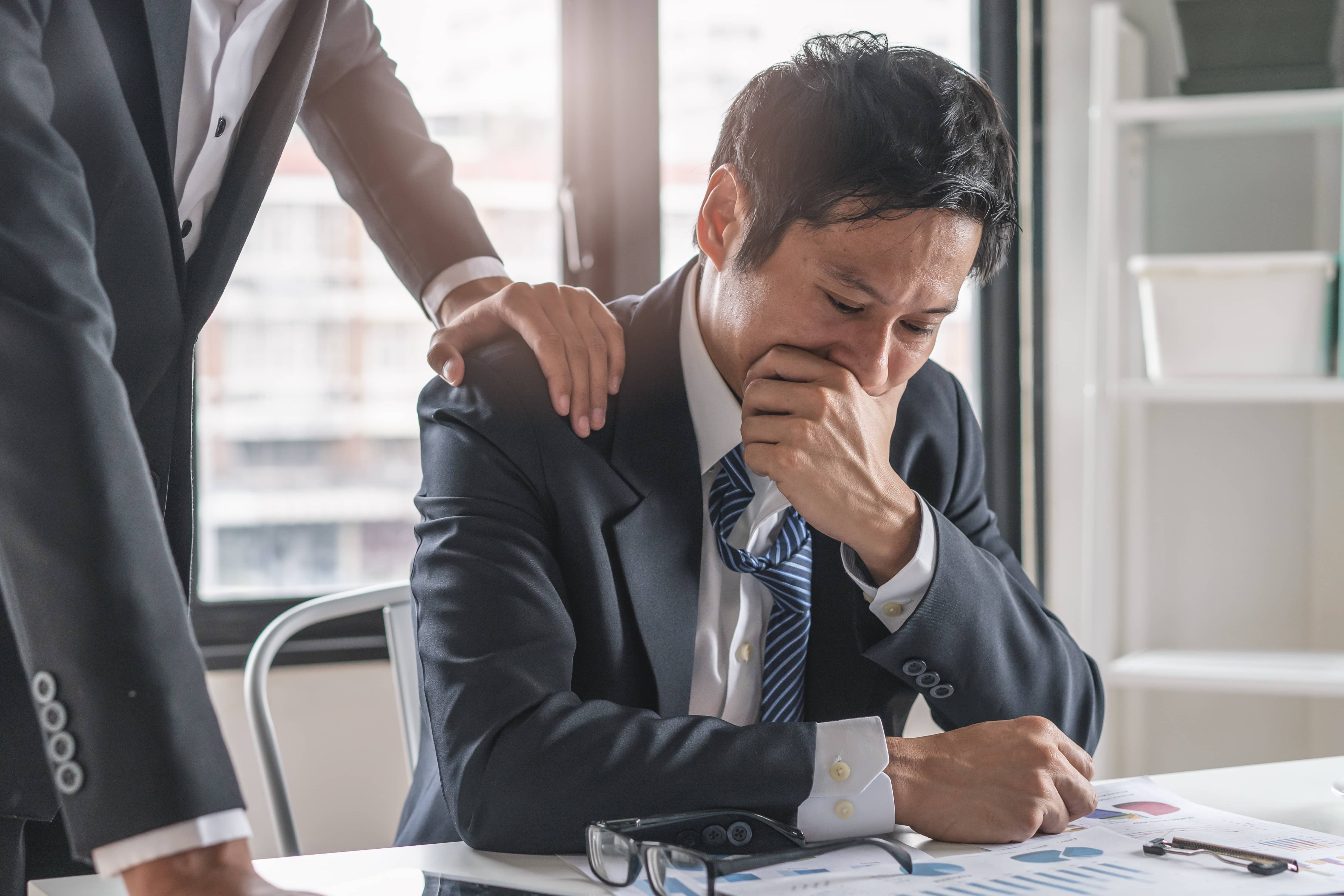 Grieving male employee with a leader's hand on his shoulder