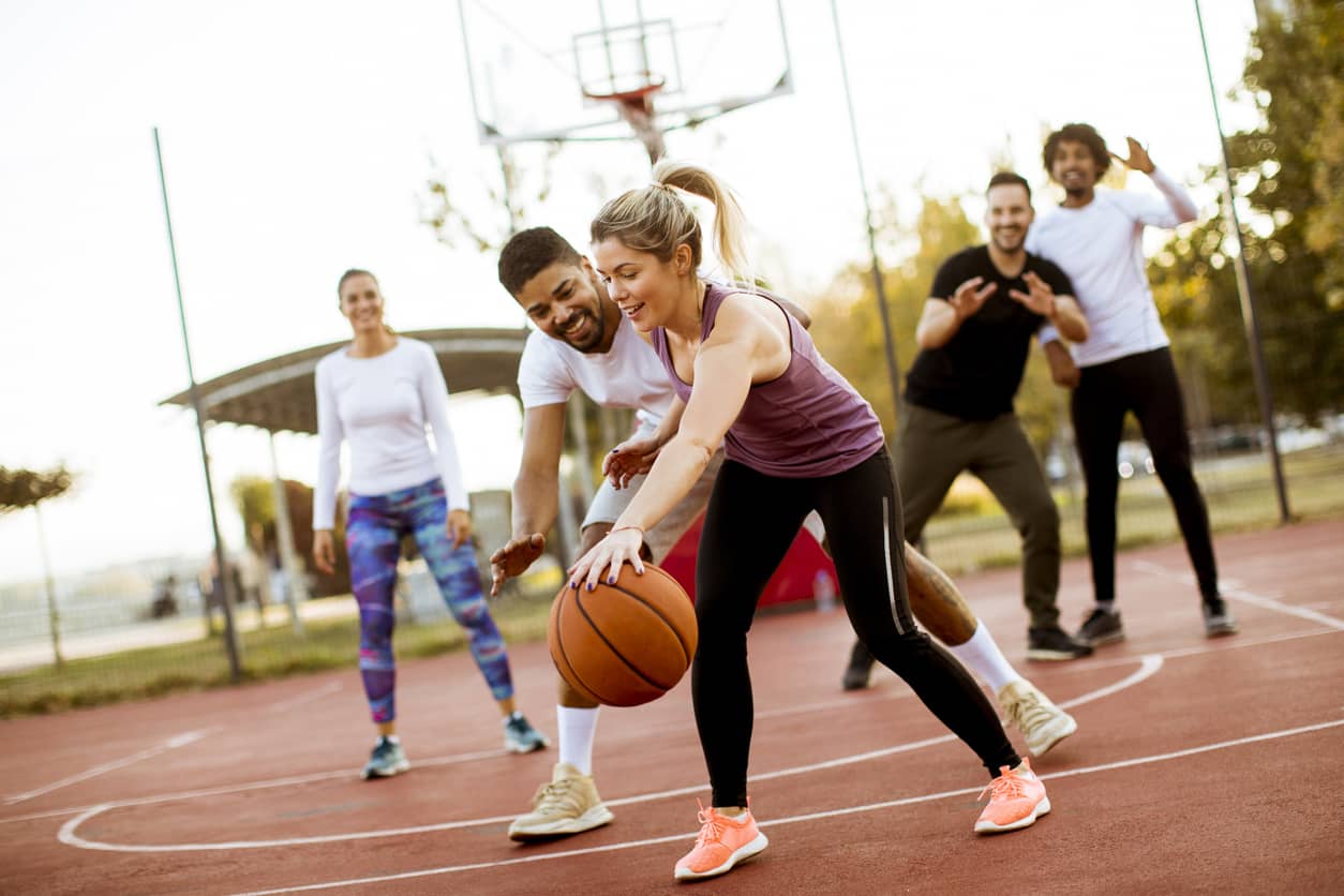 Group of multiracial young friends playing basketball outdoors.