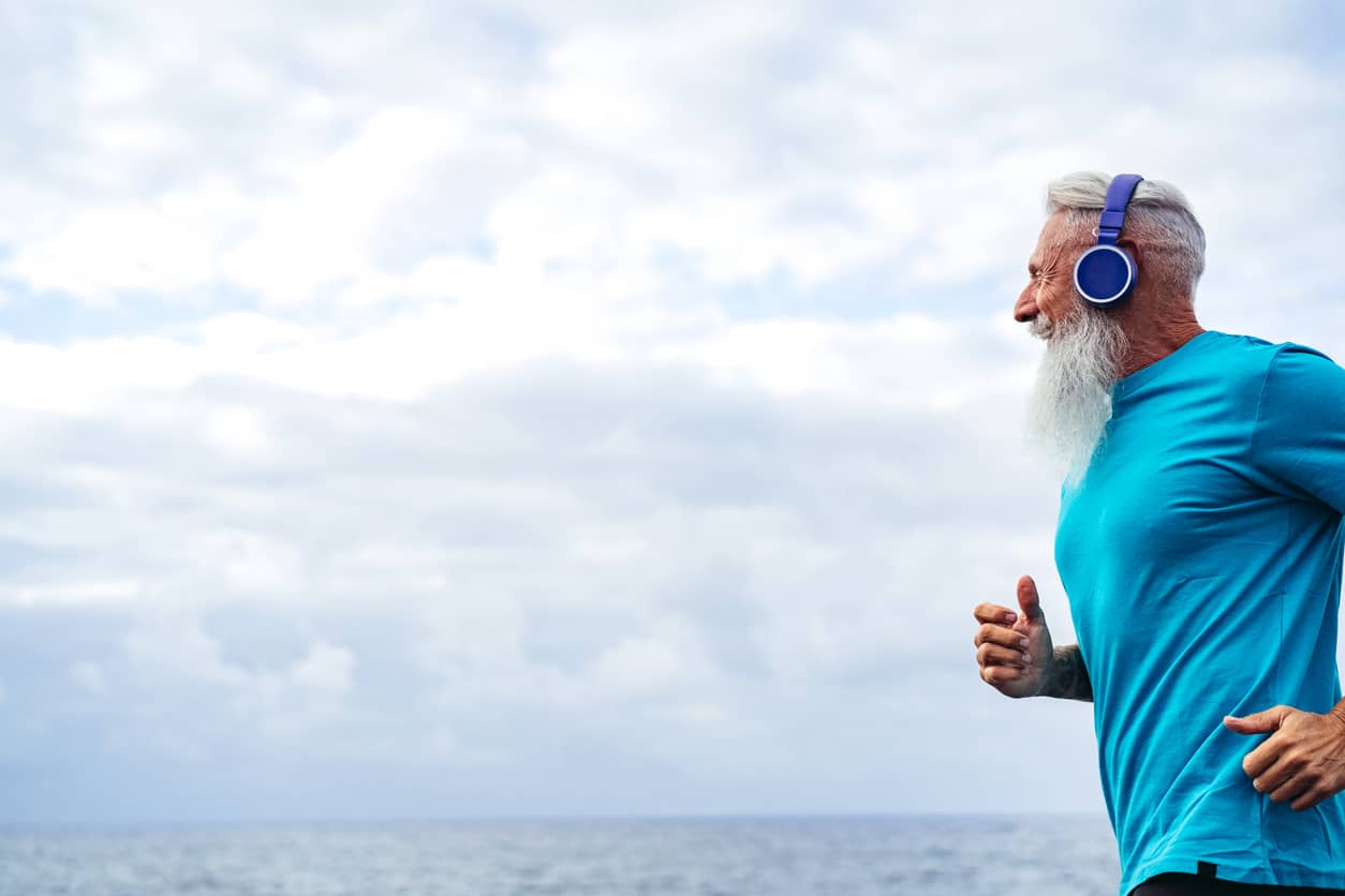 A handsome senior man with Pitta Dosha running along the ocean with a cloudy background.