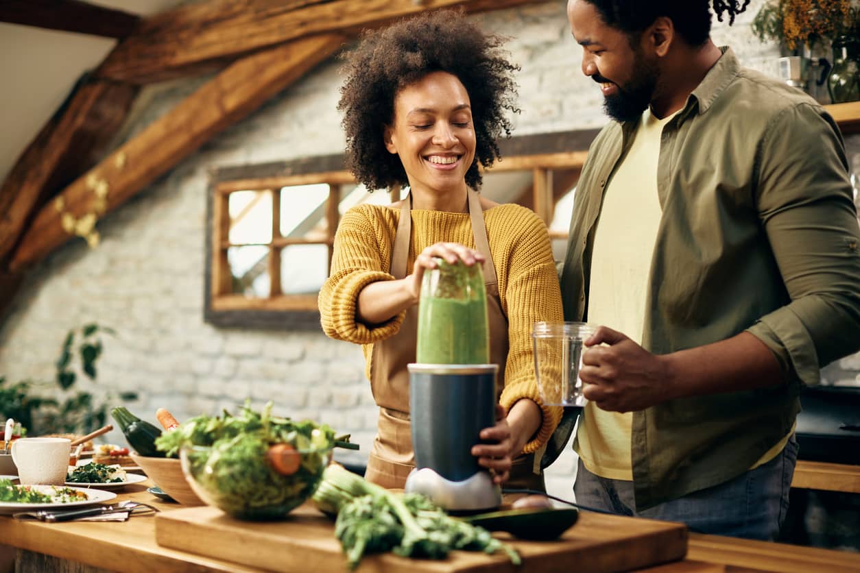 A happy African American couple blending a healthy smoothie in the kitchen.