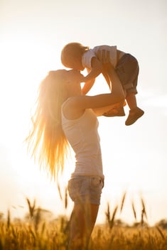 Happy mom lifting her child into the sunlit air 