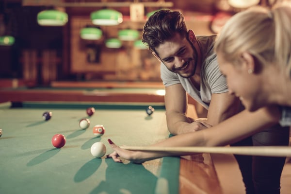 Couple playing pool with woman with the cue stick; relationship is a lot like a game of pool.