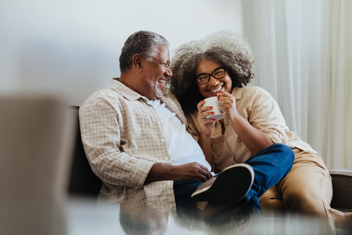 An older black couple laughing and enjoying coffee together at home.