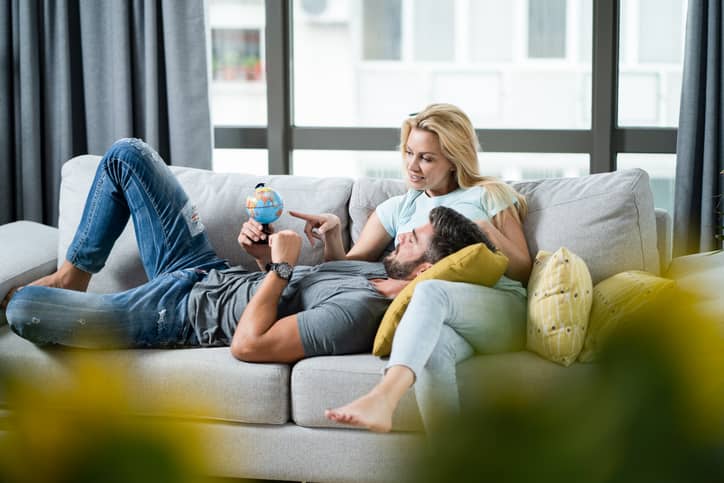 A happy young couple laying on couch looking at a globe to plan a vacation.