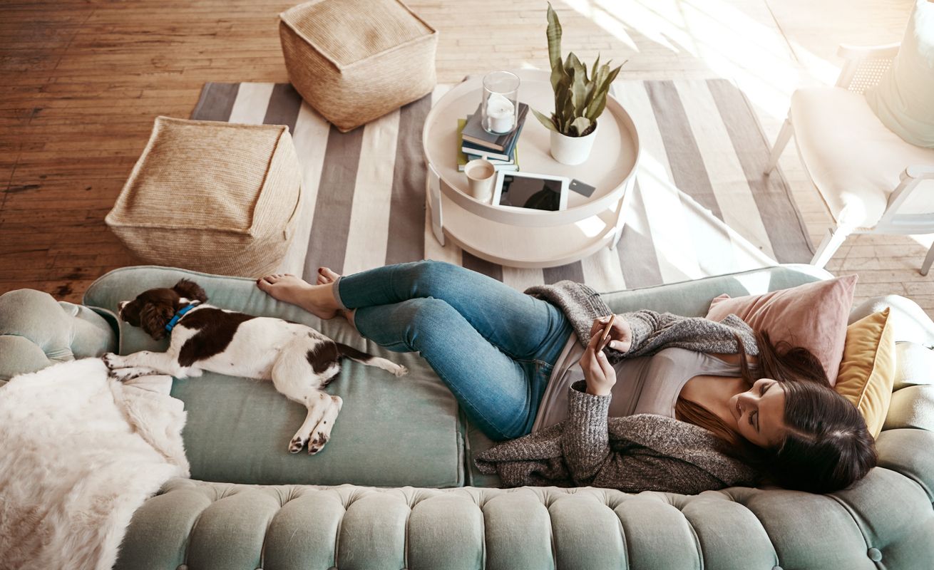 A young woman relaxing on the couch with her dog as self-care.
