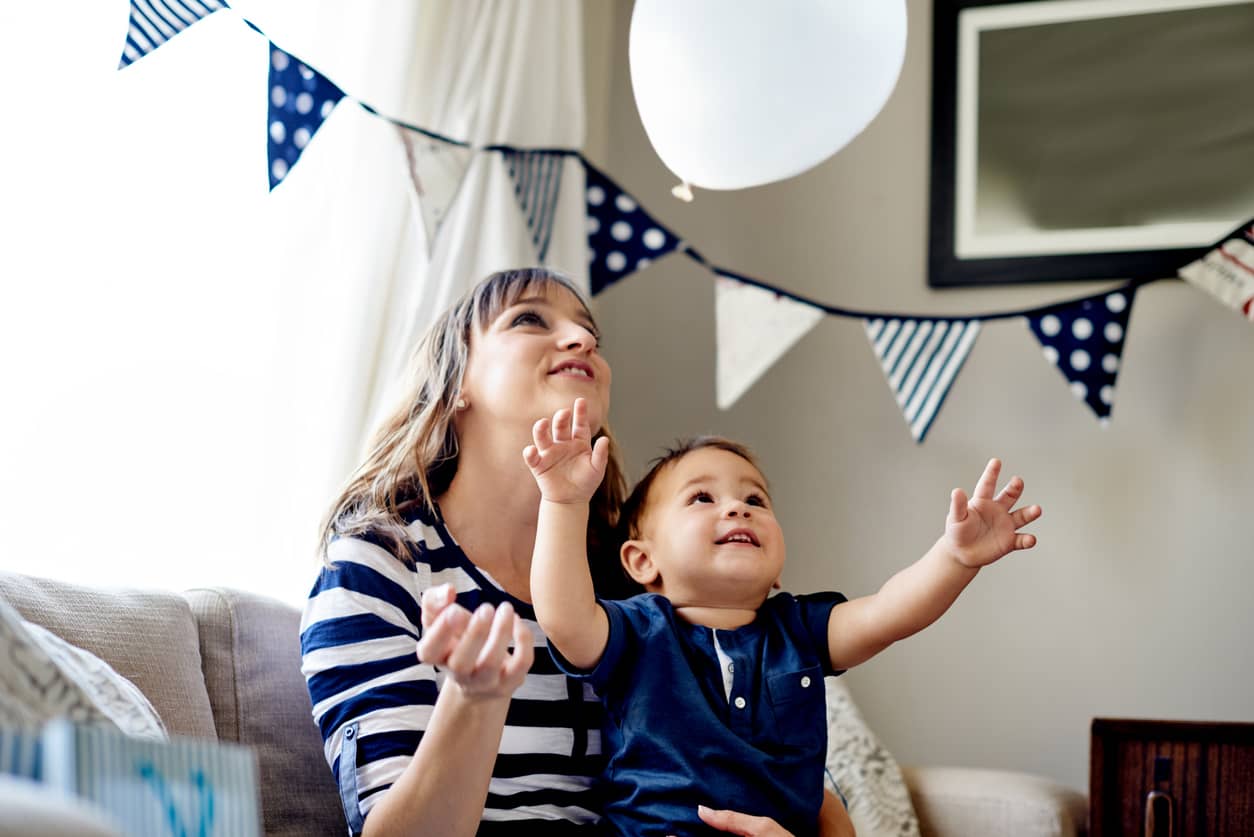 A toddler's birthday party with toddler reaching for a balloon.