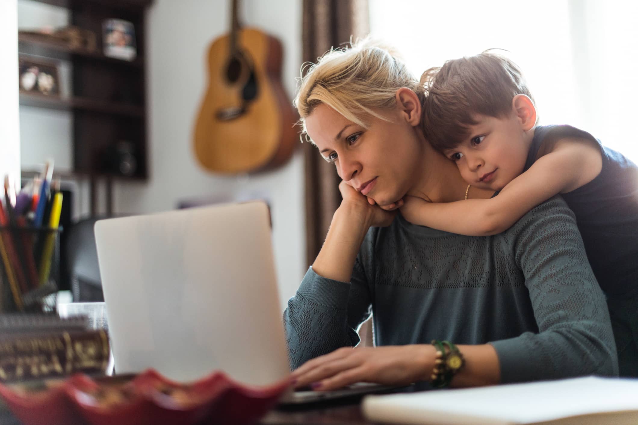 I love you mom! A preschool boy hugging his mom around the neck from behind as she works on a computer.