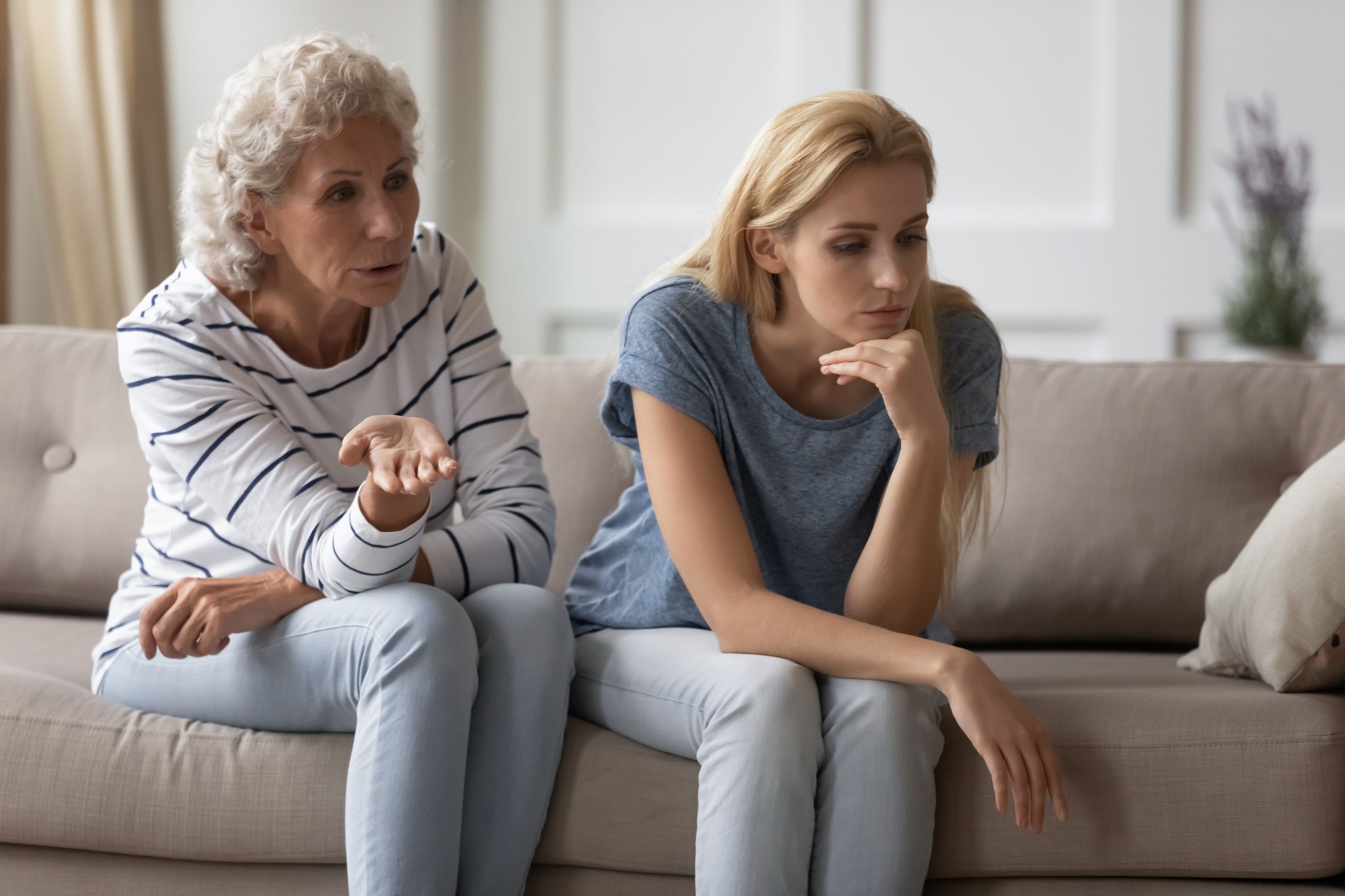 It is your fault. Unhappy sad young woman with mother criticizing her while both sit on sofa.