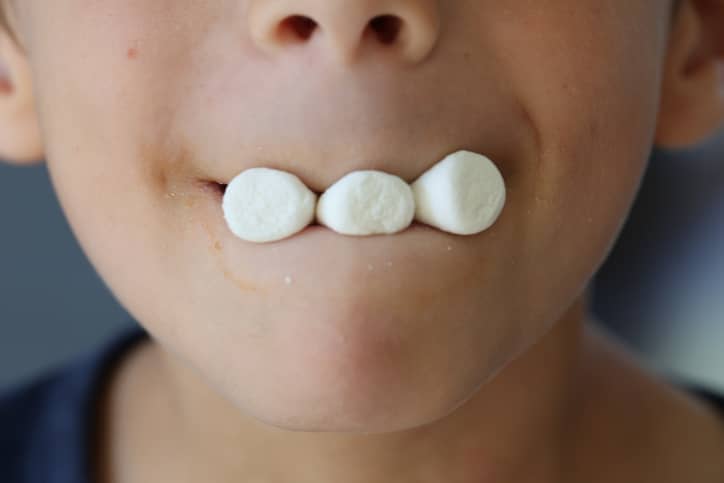 A boy holding multiple marshmallows in between his lips.