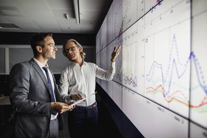 Two men reviewing a large interactive screen and measuring results.