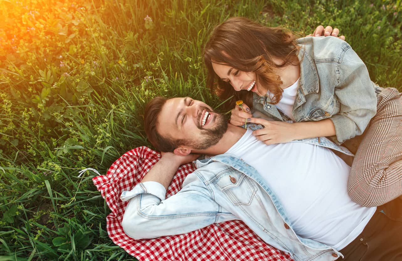 Laughing couple laying on a checkered blanket on green grass.