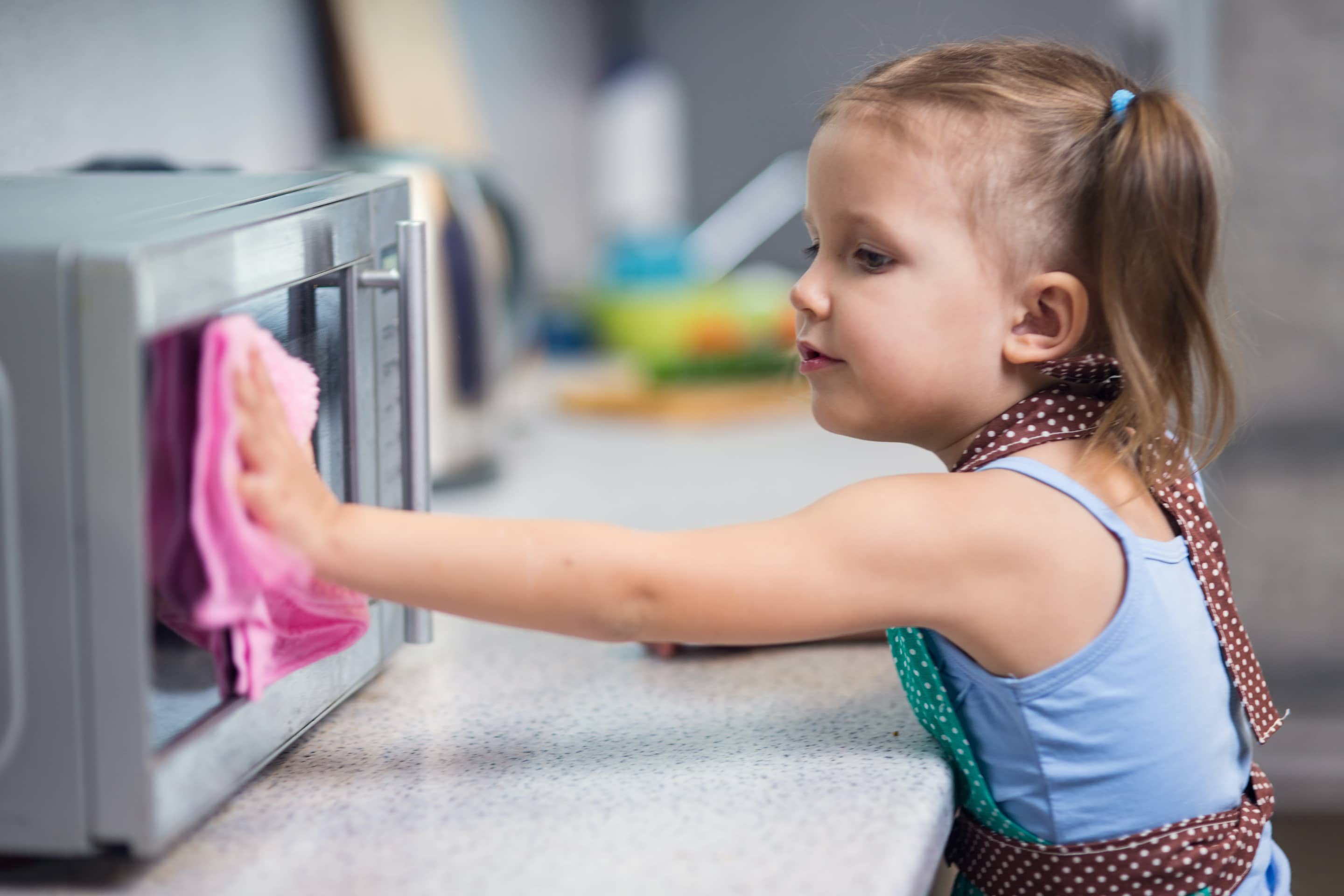 Young girl wiping the toaster oven in the kitchen.