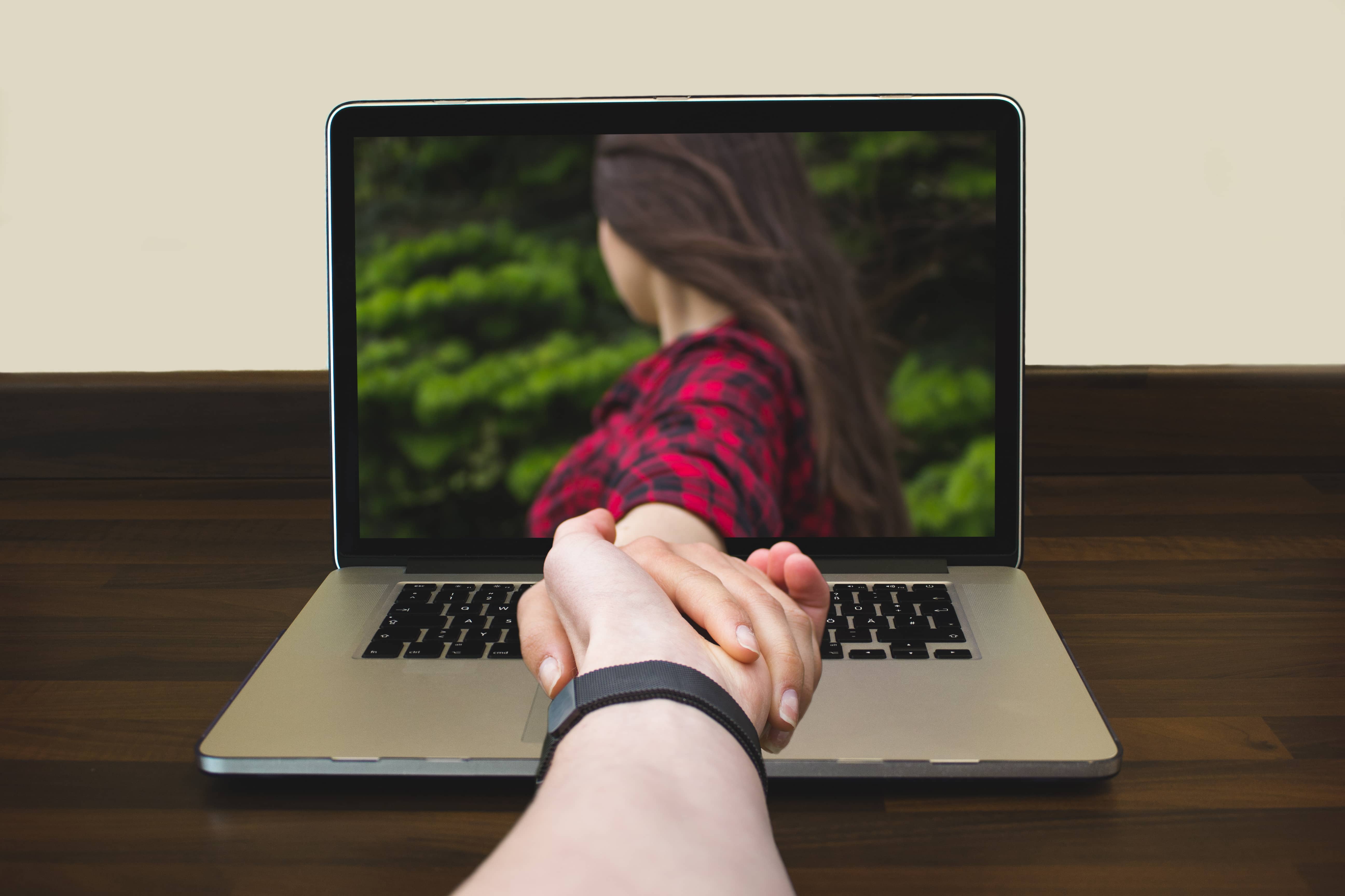 Long distance relationships with hand reaching through a computer screen.
