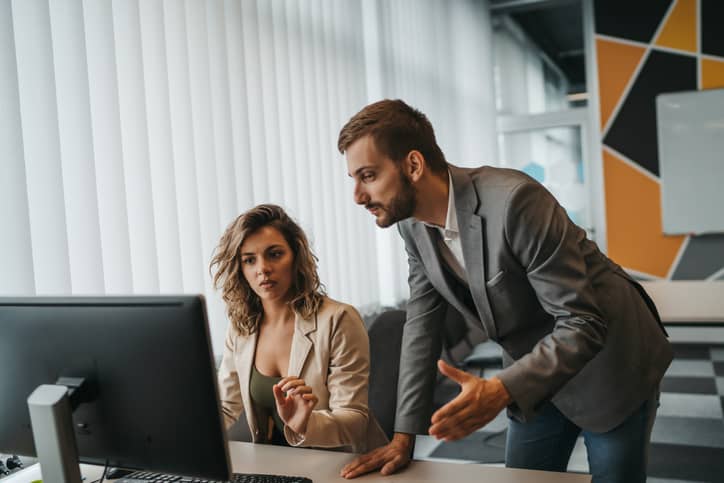 An autocratic leader reprimanding an employee who sits at a computer.