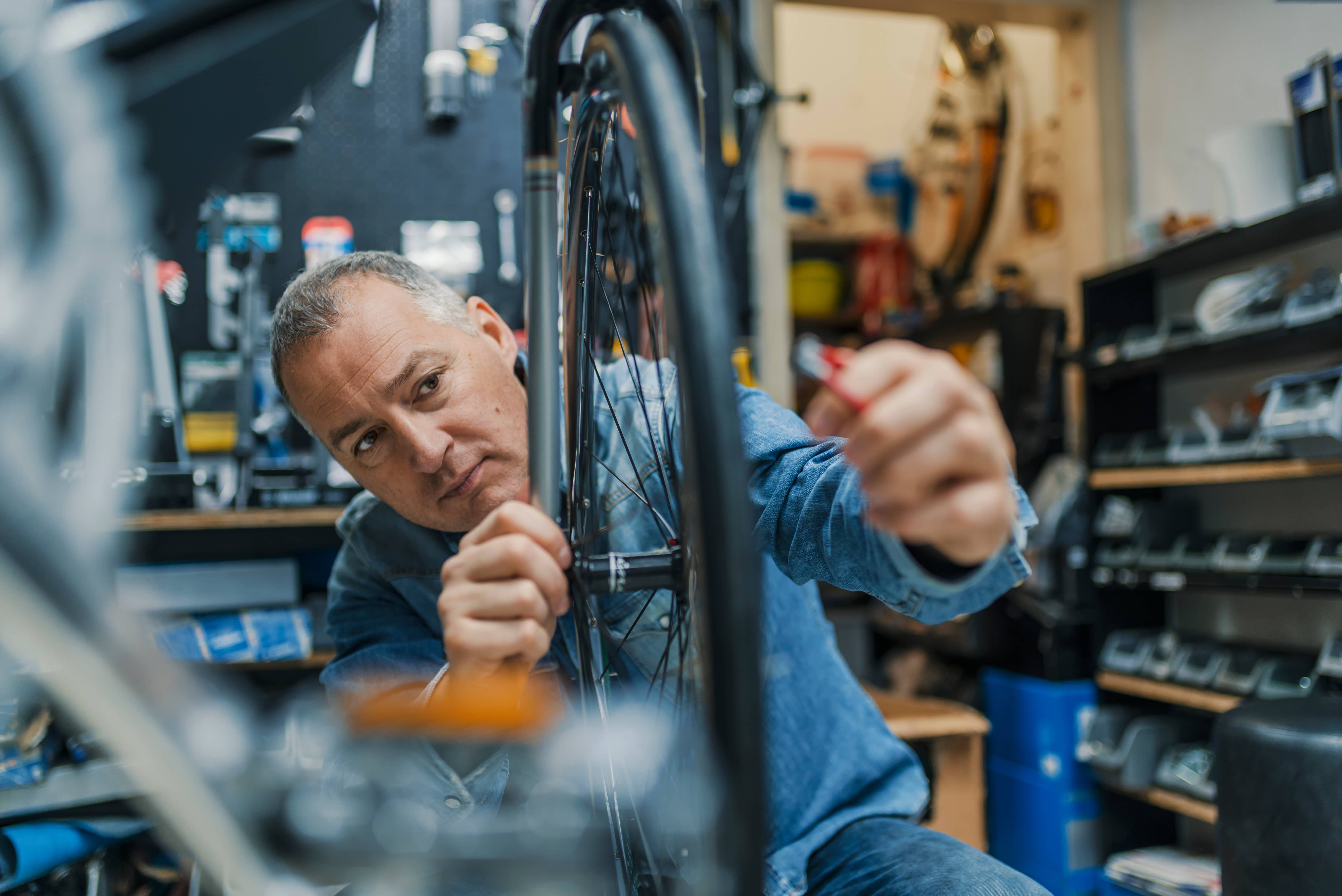 An middle-aged man fixing and balancing a bike wheel.