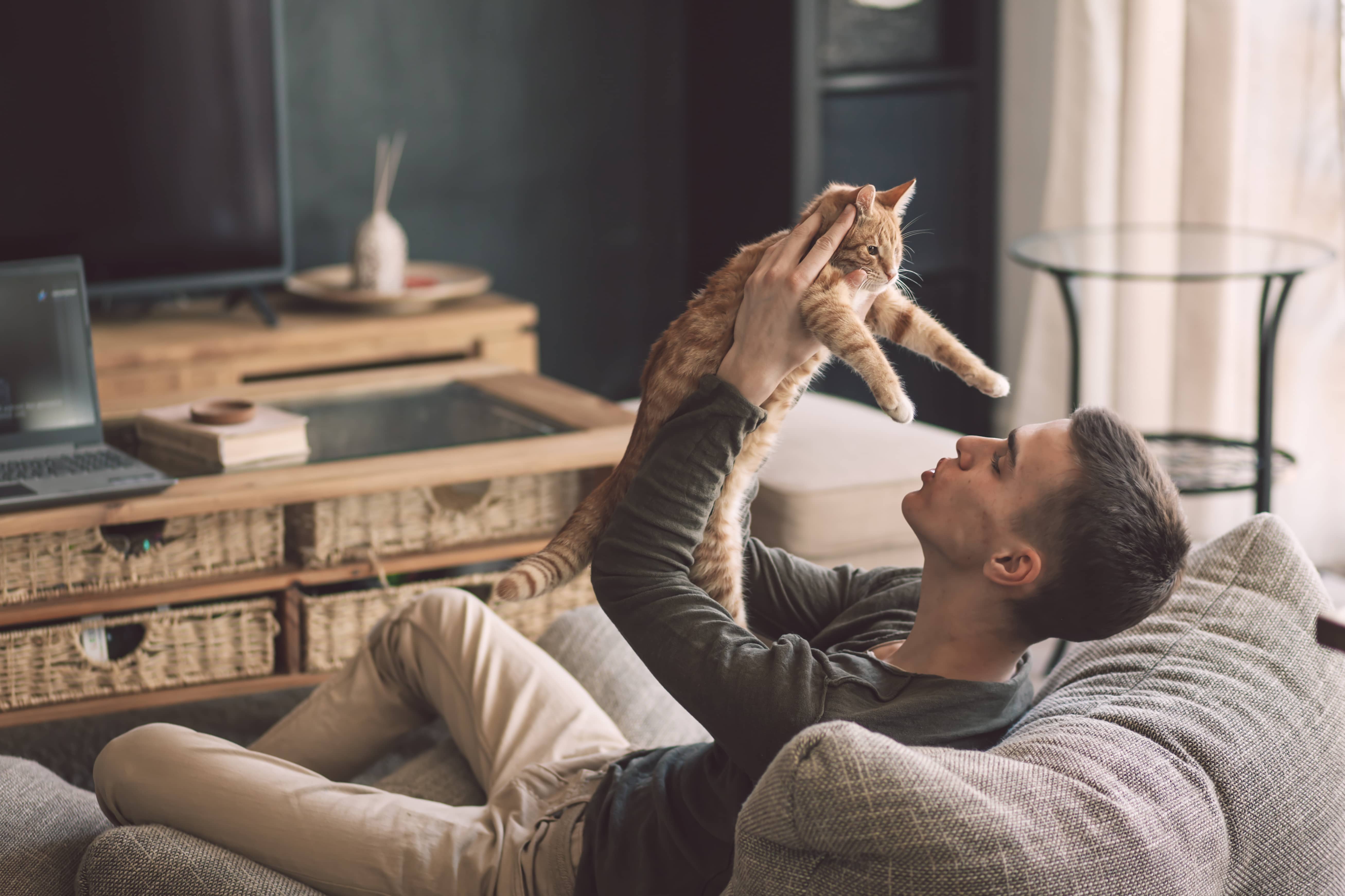 Young man holding up a cat affectionately