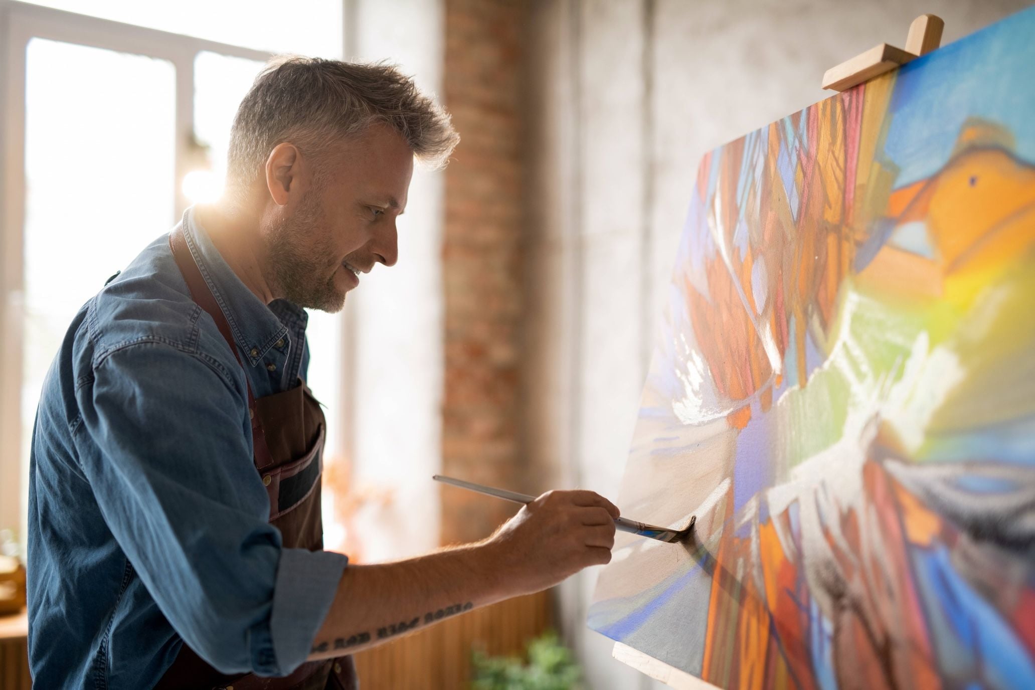 Man painting with acrylics with sunshine in coming through the window.
