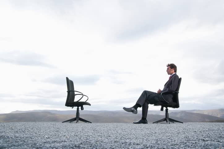 Man sitting in office chair facing empty chair representing a lack of leadership, interaction and feedback.