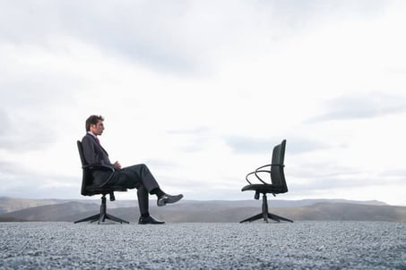 Man sitting in office chair facing empty chair representing a lack of leadership, interaction and feedback.