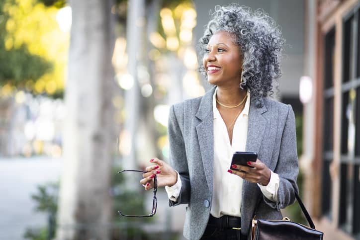 Mature happy black woman texting while walking in a city.