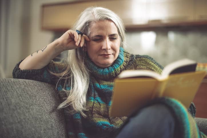 Mature woman reading a book on her couch at home.