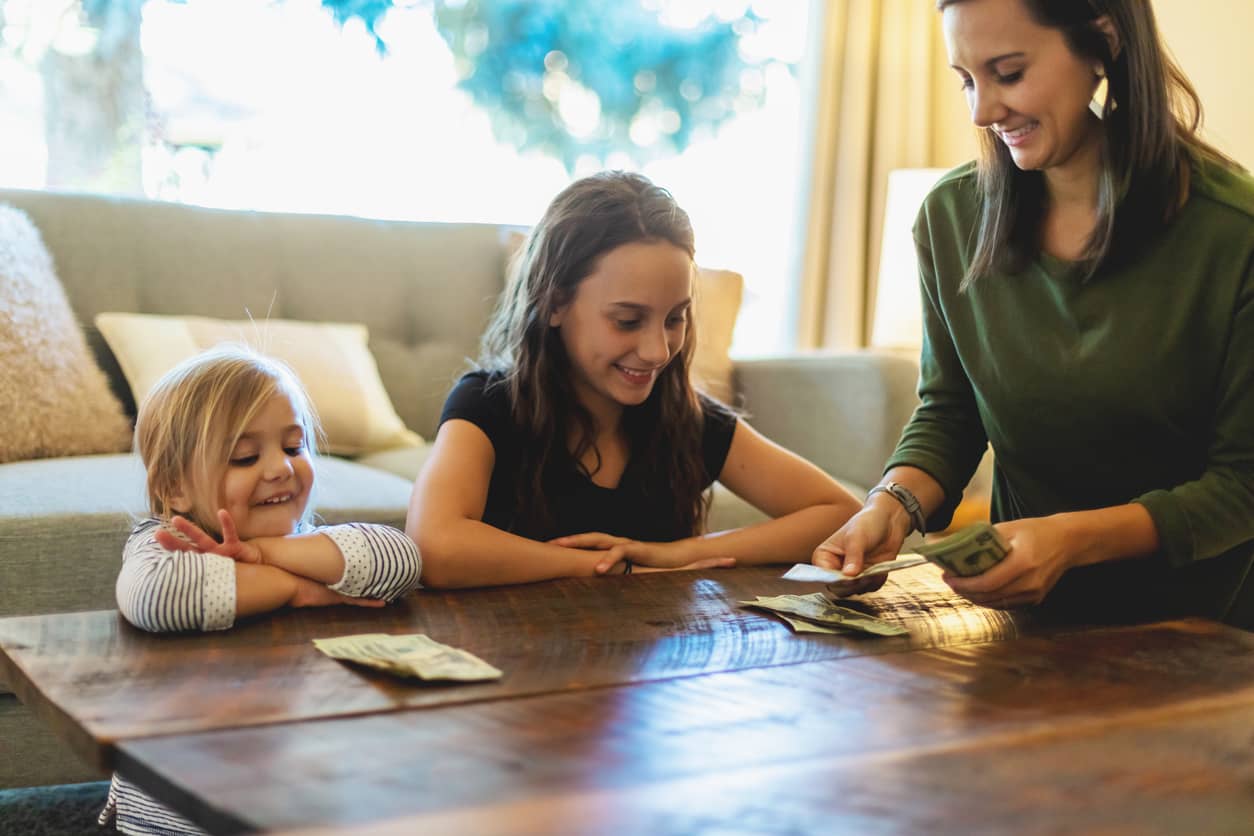 A millennial mother discussing money with her teenage and preschool daughters.