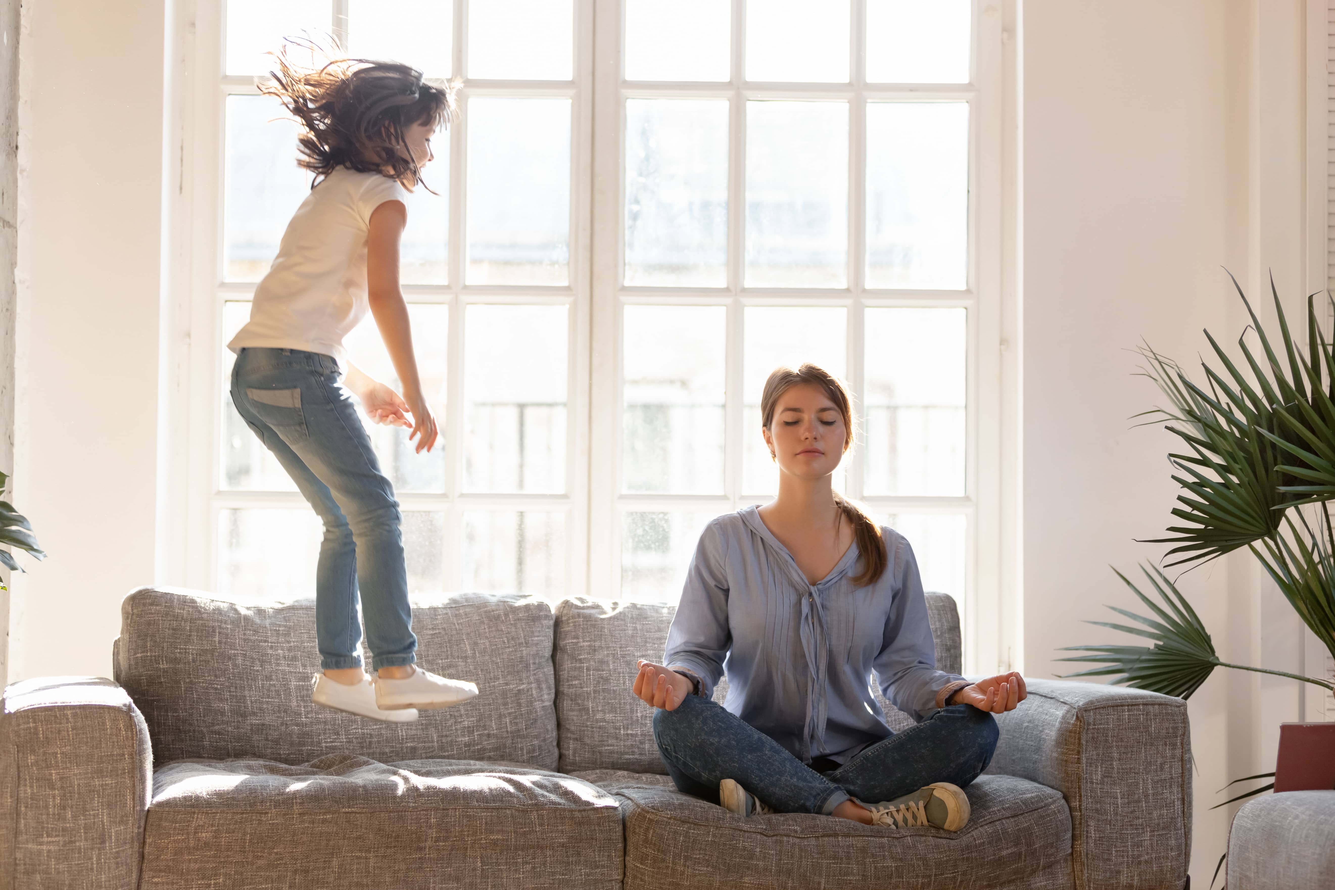 Mom in mindfulness practice as young girl jumps on couch