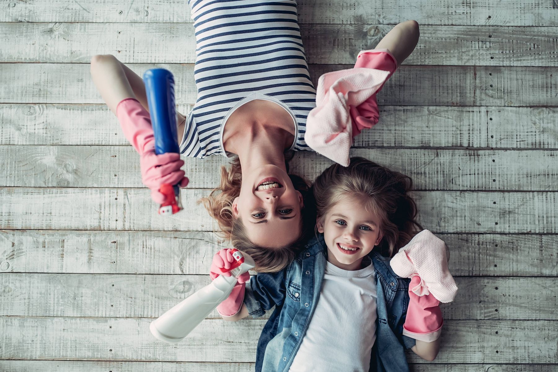 Mother and daughter laying on floor with cleaning rags having fun with chores.