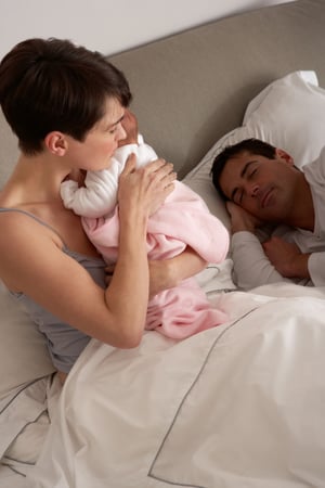 Mother comforting newborn while her spouse sleeps