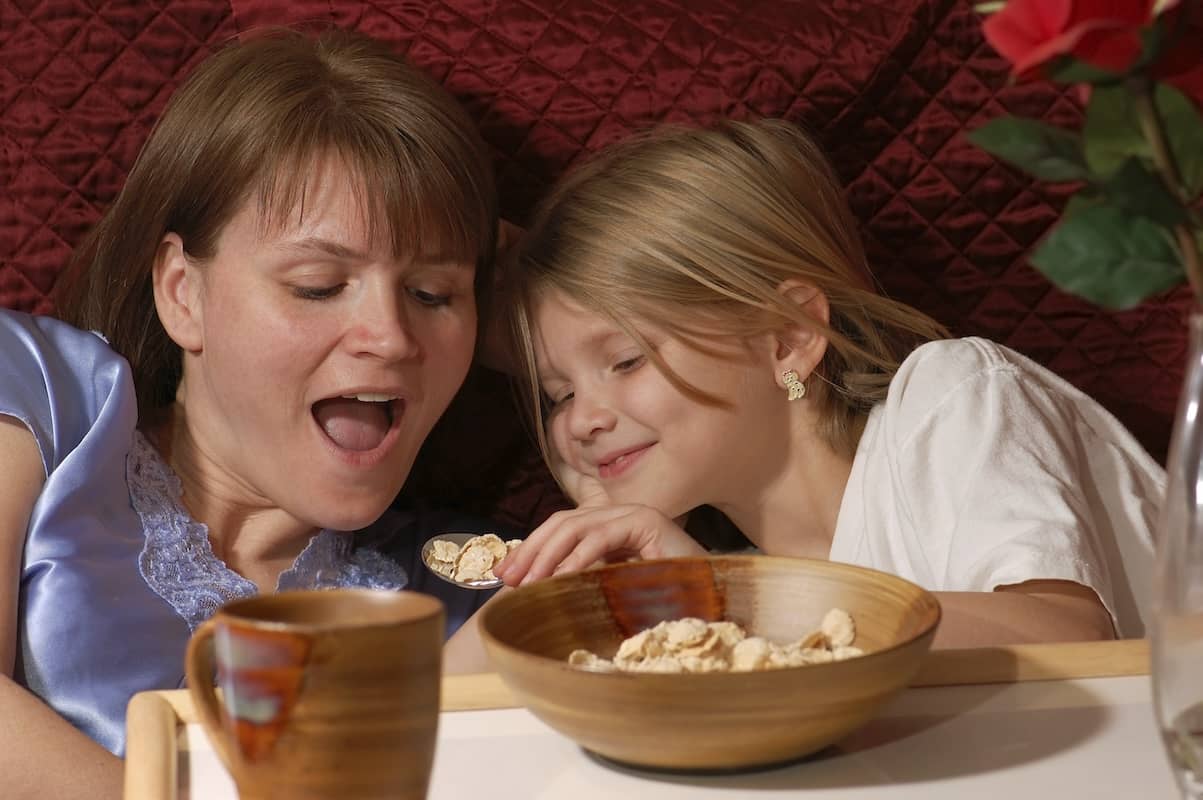 Mothers Day breakfast with a mother and daughter in bed eating a bite together..