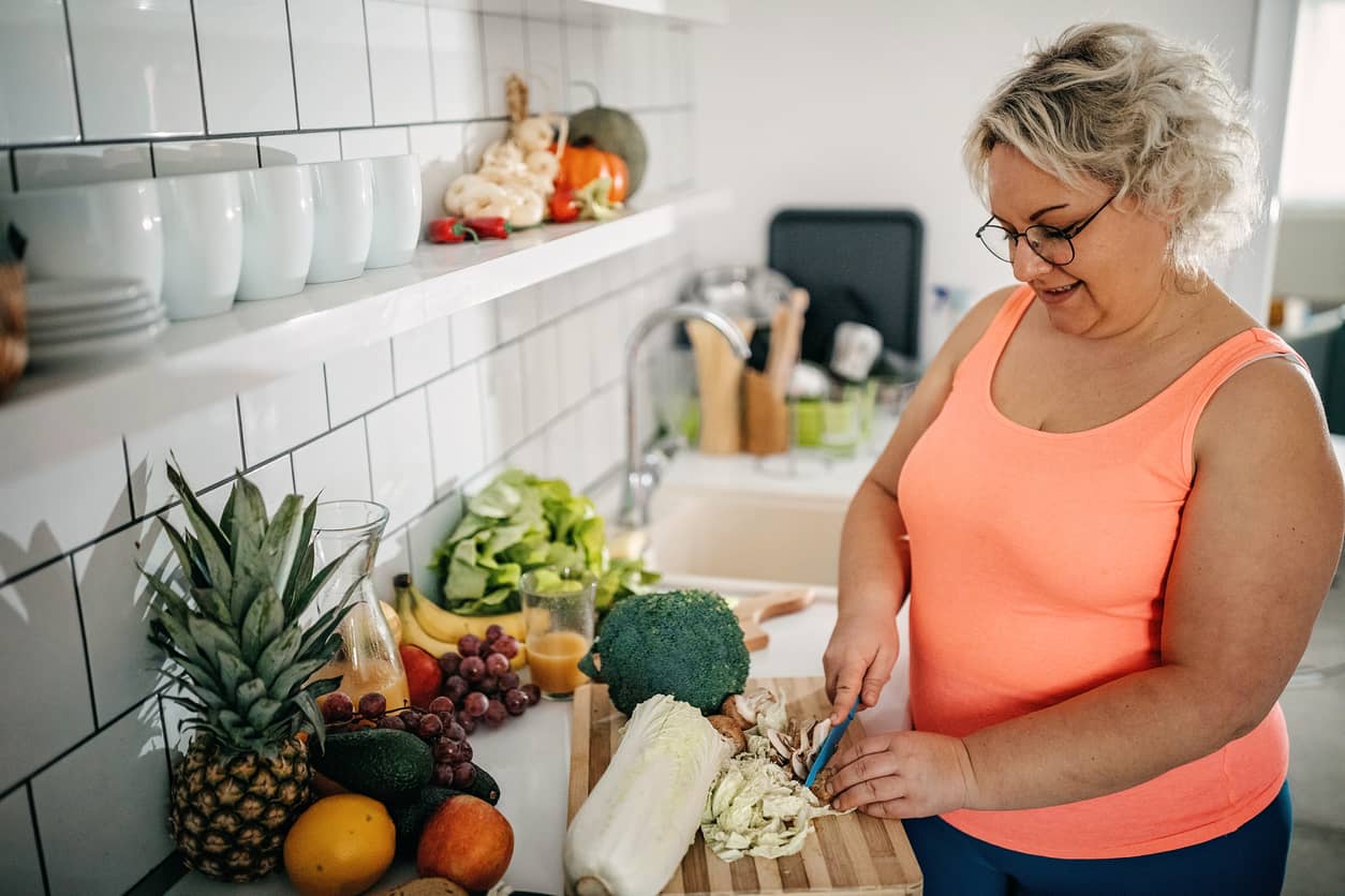 A chubby woman chopping vegetables for her weight loss plan.