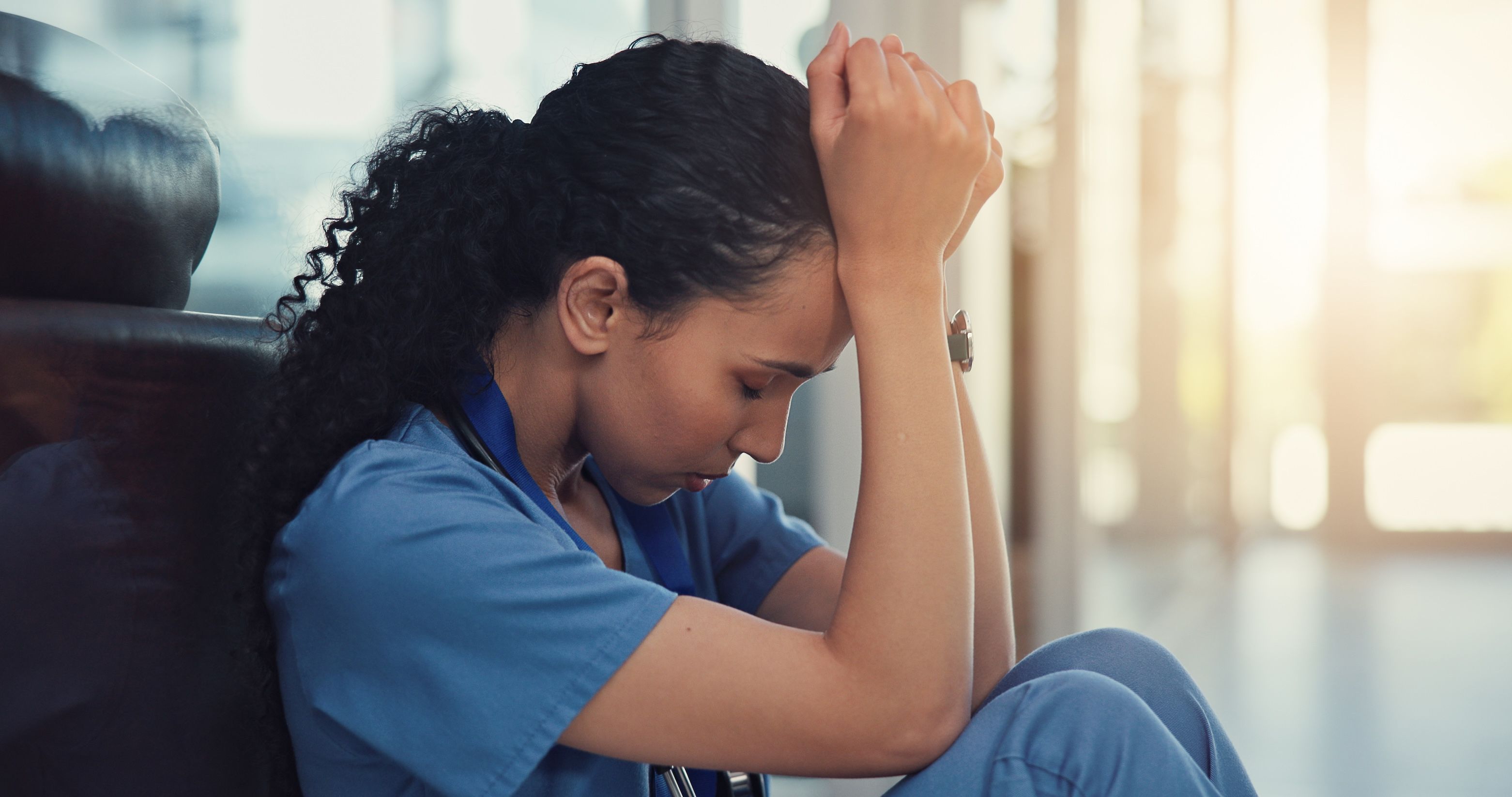 A nurse sitting with her head in her hands stressed, anxious, overwhelmed and burned out at a health clinic.