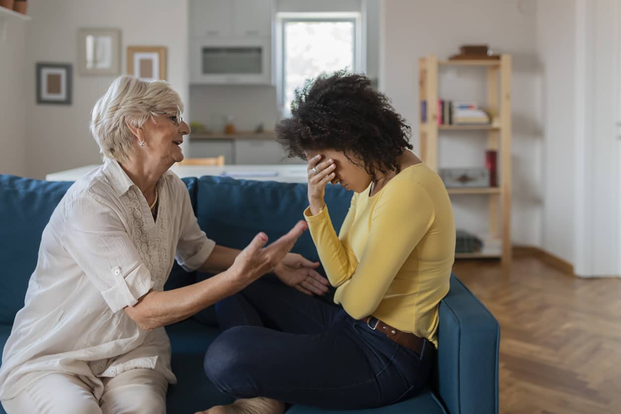 A fragile mother upset with her grown daughter who has her face in her hands.