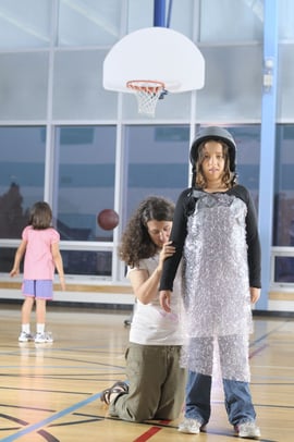 A overprotective mom has her elementary daughter on the basketball court wrapped in bubblewrap.