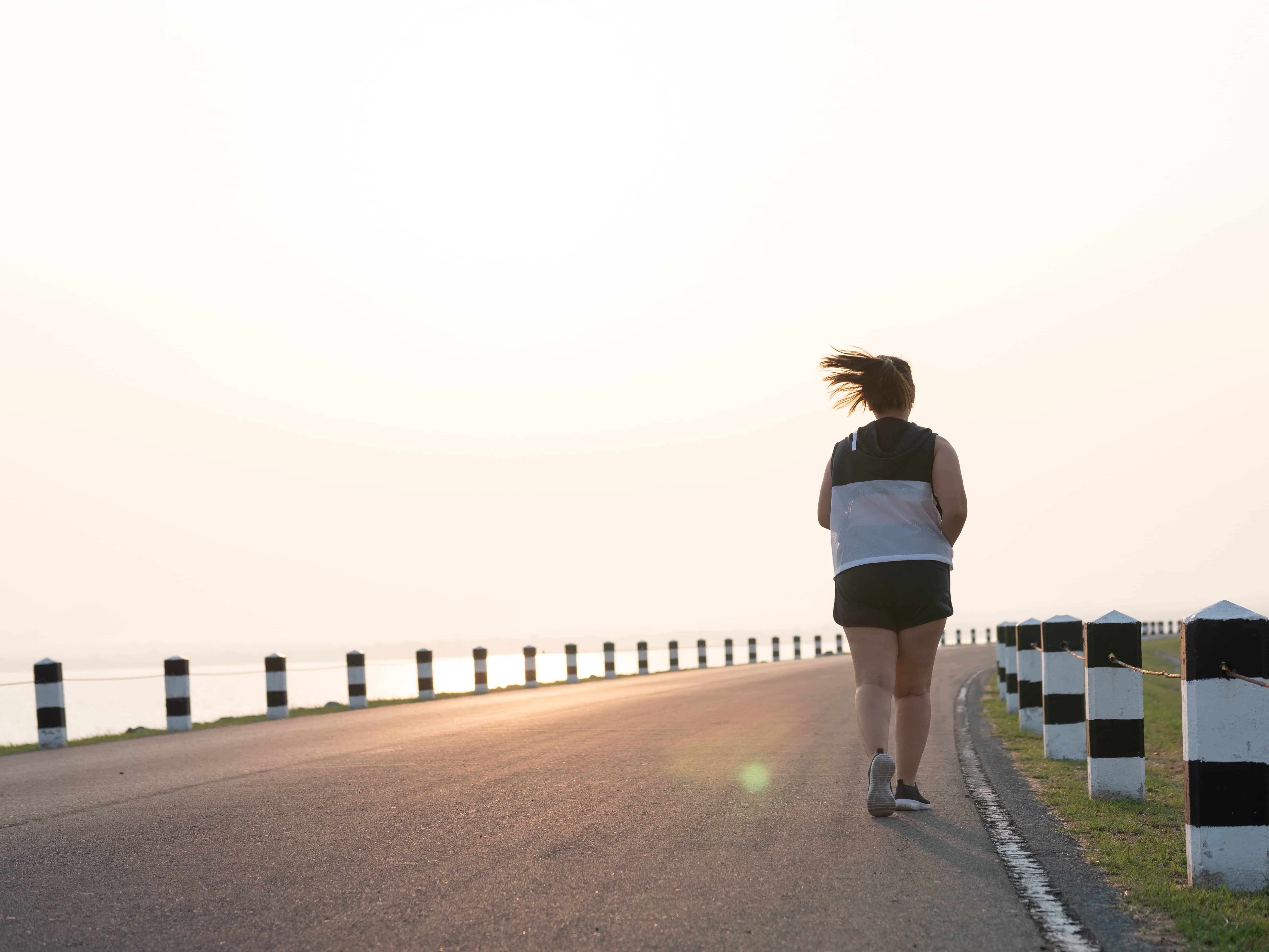 A women with Kapha Dosha jogging on a road next to the ocean; cardio and regular exercise is vital for Kapha Doshas