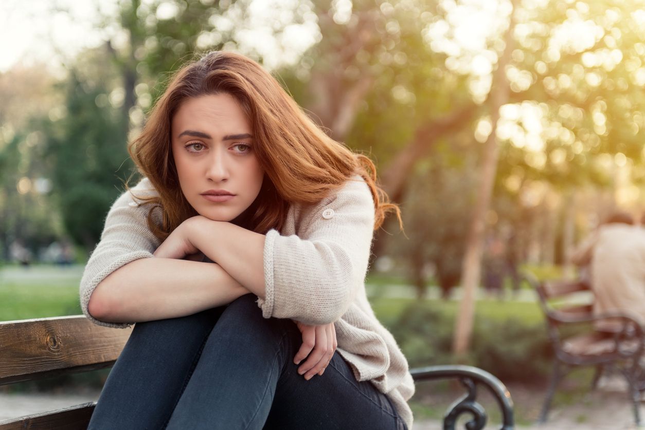 A young woman sitting on a part bench who is depressed with emotional blocks.