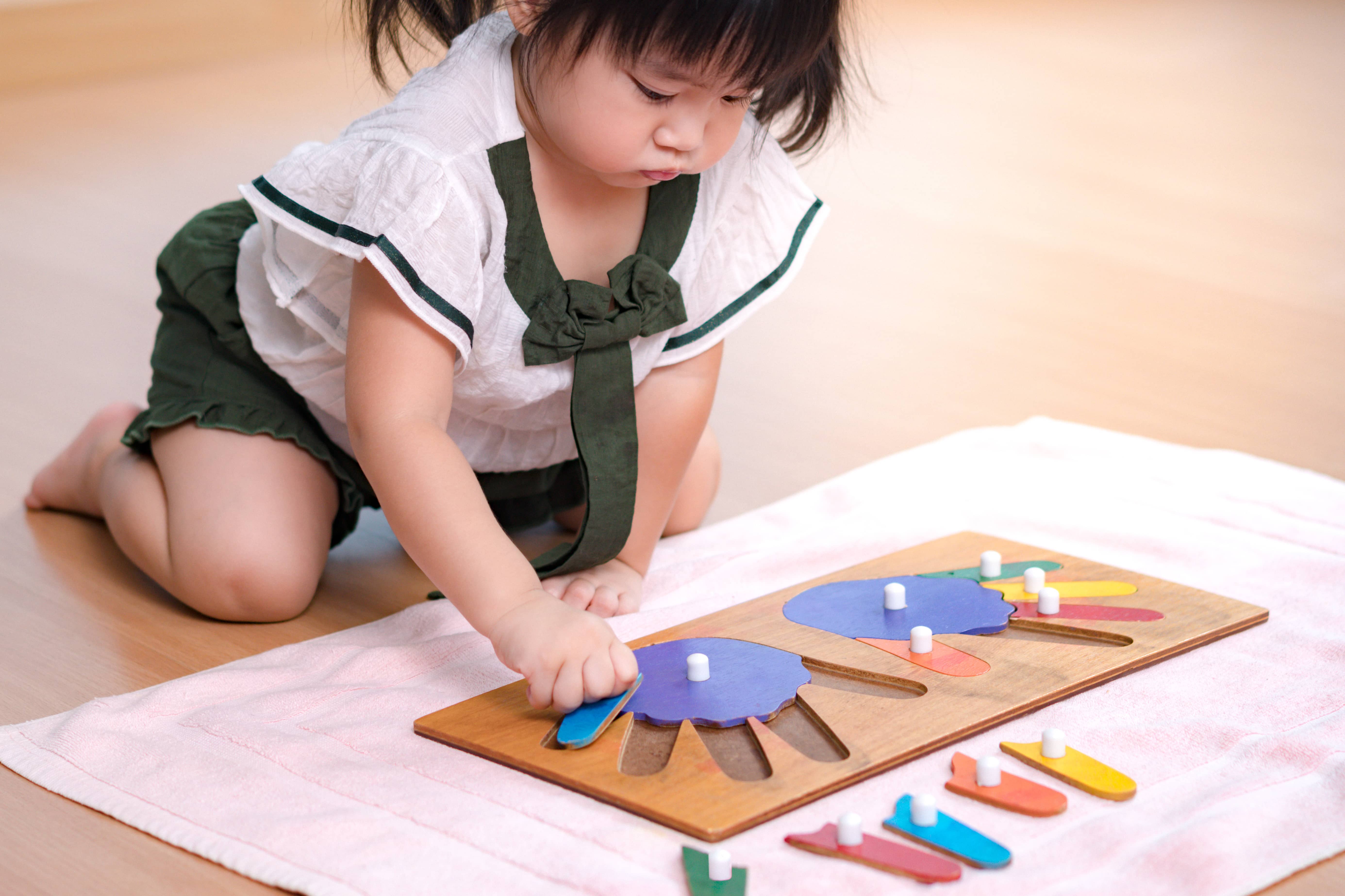 An Asian preschool girl assembling a hand puzzle in her Montessori at Home