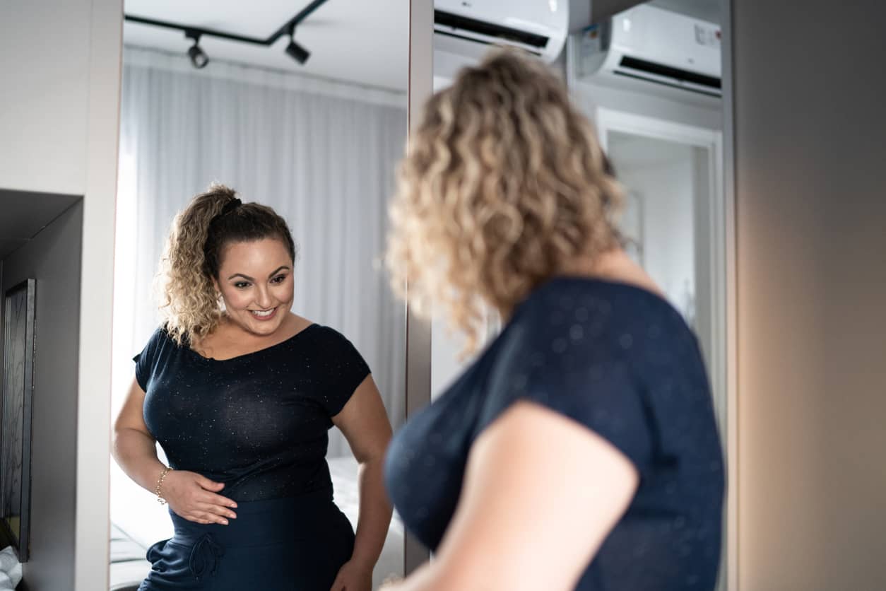 Pretty woman getting dressed up and looking in the mirror pleased with her weight loss.