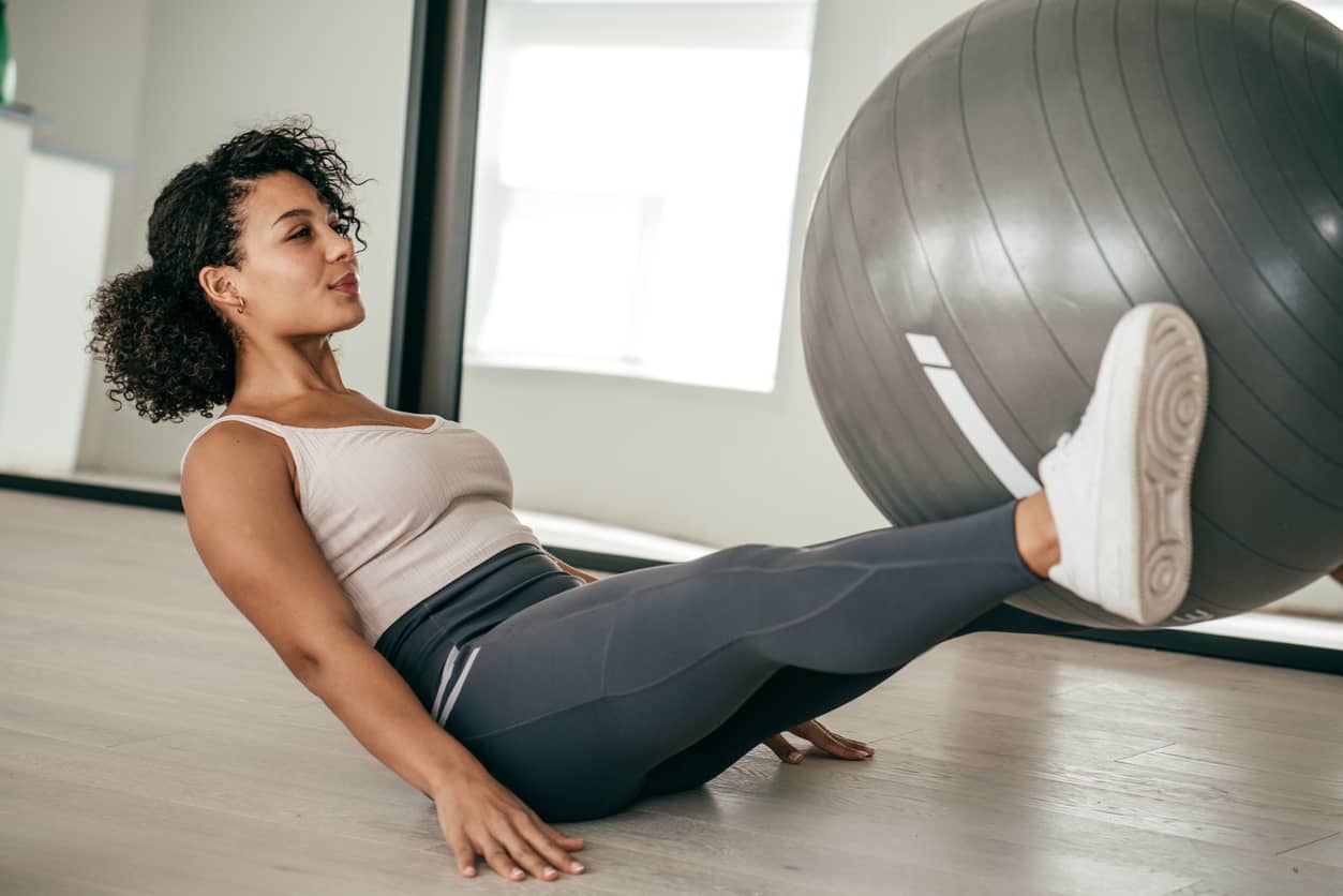 Woman holding a large ball between her legs and raising them. Self-care translates to self-love.