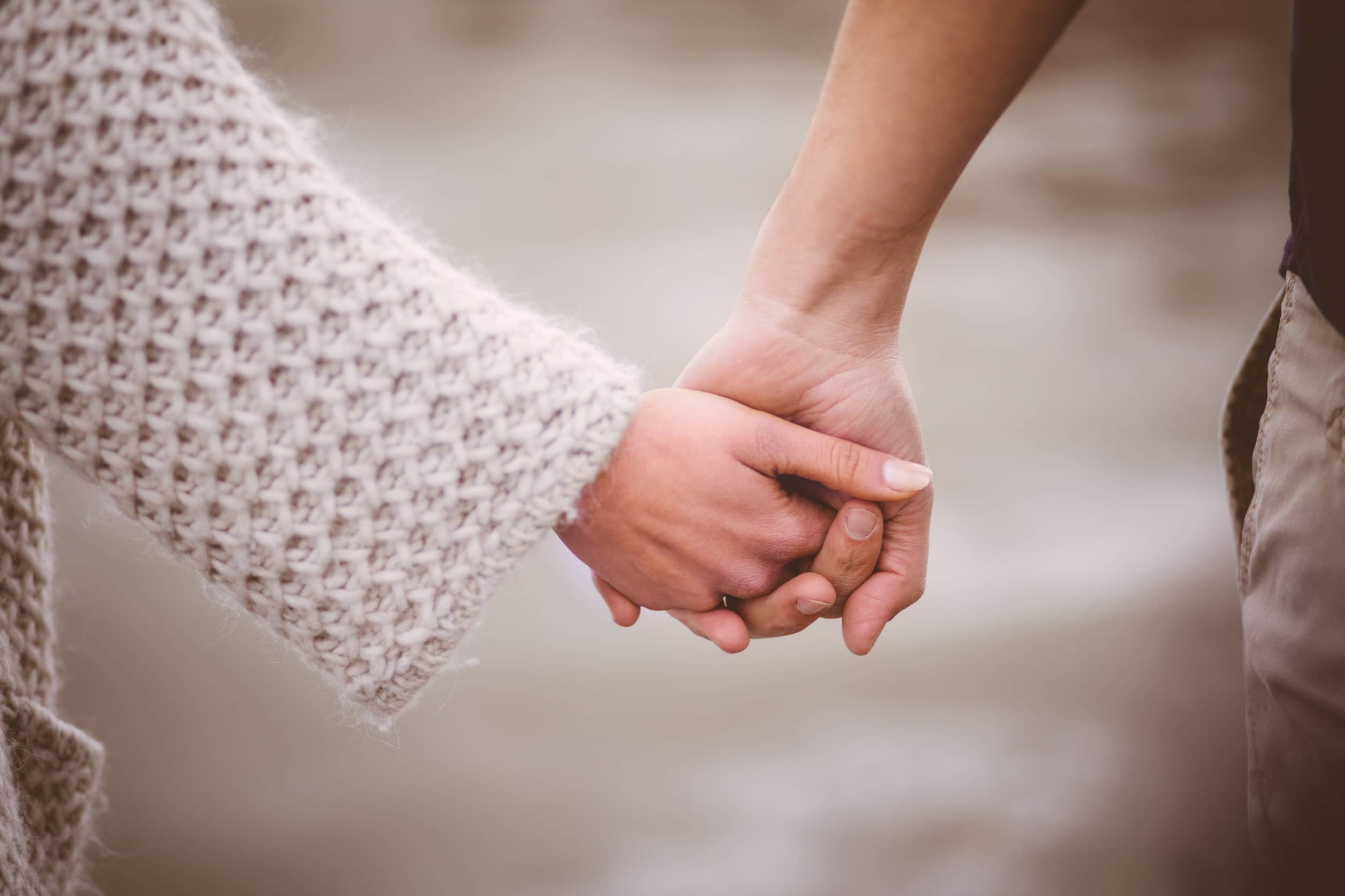 A romantic couple tenderly holding hands on a walk outdoors.